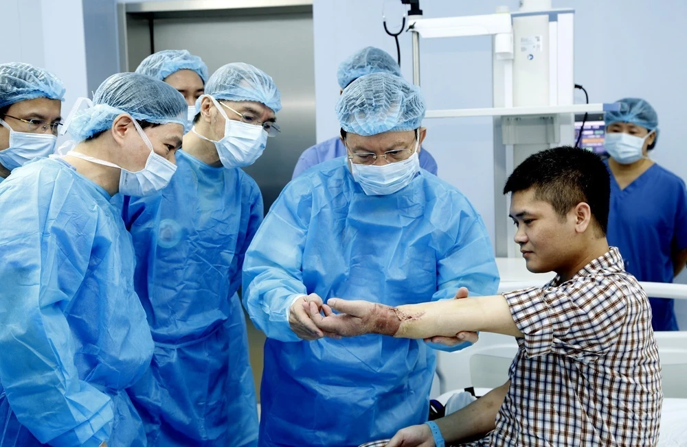 Các y bác sỹ Bệnh viện Trung ương Quân đội 108 kiểm tra tay cho bệnh nhân Vương sau khi ghép. (Ảnh: PV/Vietnam+)