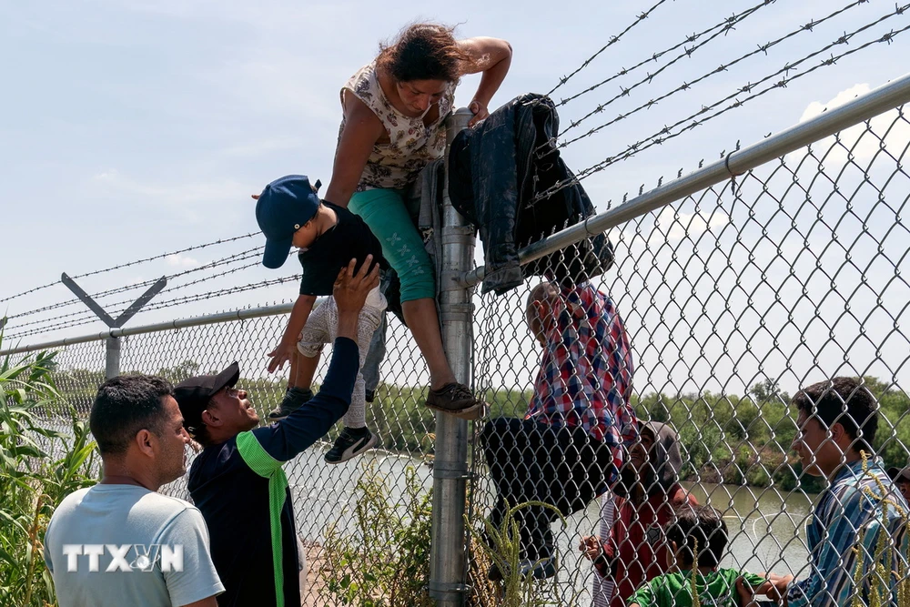 Người di cư từ Mexico trèo qua hàng rào biên giới tại Eagle Pass, bang Texas để vào Mỹ. (Ảnh: AFP/TTXVN)