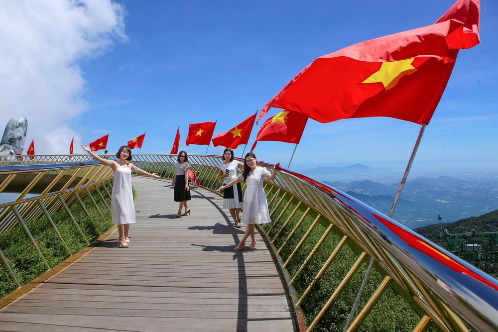 Giới trẻ thích thú được check-in trên Cầu Vàng với dãy cờ Tổ quốc tung bay. (Ảnh: Trần Lê Lâm/TTXVN)