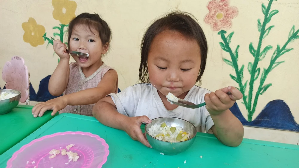 Bữa ăn bán trú của học sinh điểm trường Sáng Xoáy. Không có điện, để thoáng mát, các em ăn bữa trưa ở ngay hàng lang lớp học. (Ảnh: Phạm Mai/Vietnam+)