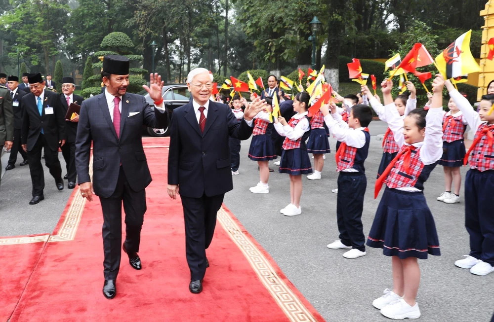 Tổng Bí thư, Chủ tịch nước Nguyễn Phú Trọng và Quốc vương Brunei Hassanal Bolkiah vẫy chào thiếu nhi Việt Nam tại lễ đón. (Ảnh: Trí Dũng/TTXVN) 