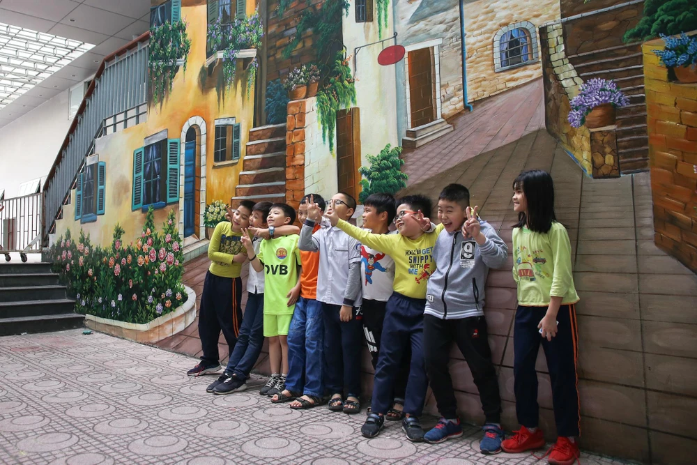 Các bạn học sinh trường Tiểu học Dịch Vọng B hồn nhiên vui đùa cùng những bức tranh tường độc đáo. (Ảnh: Quang Sỹ/Vietnam+)