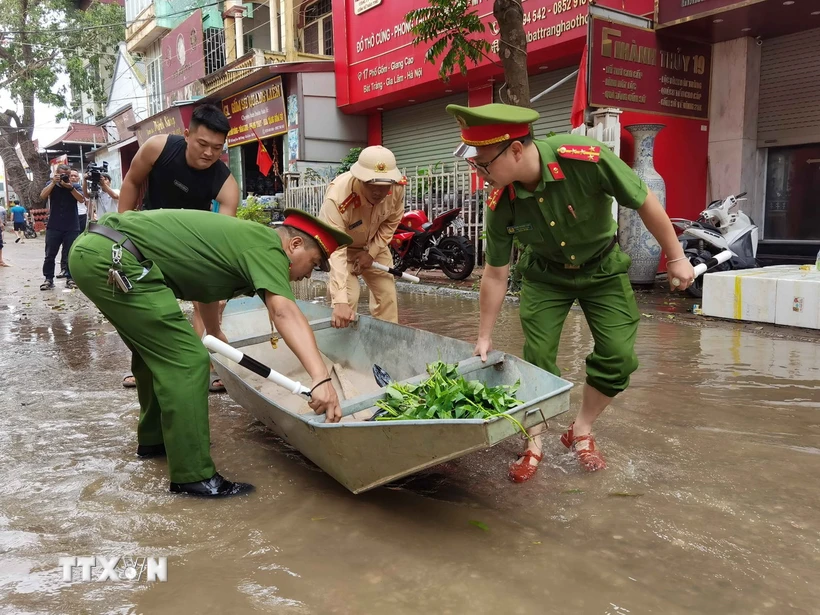 Lực lượng công an hỗ trợ thuyền nhỏ để giúp người dân di chuyển trong vùng lụt. (Ảnh: Thanh Tùng/TTXVN)