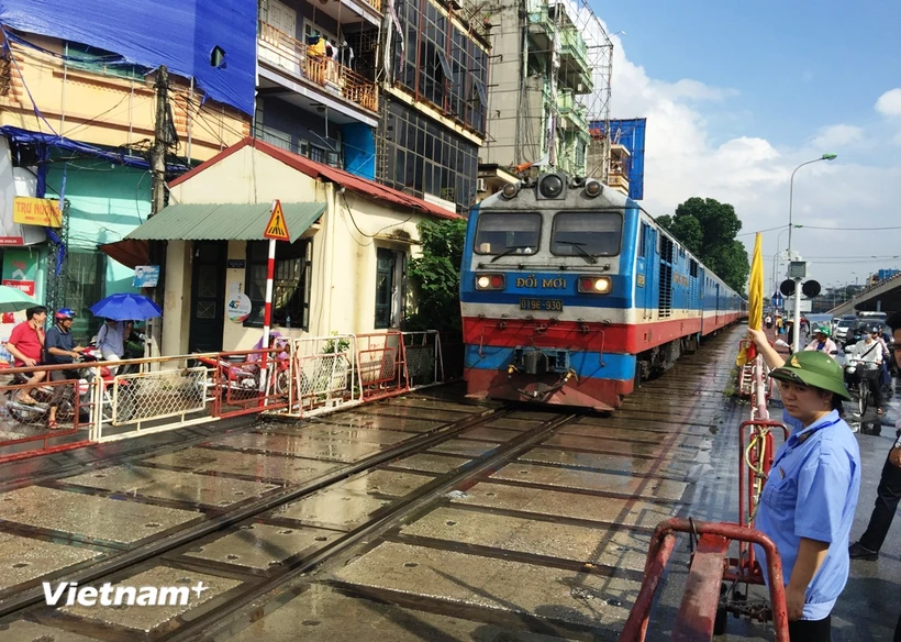 Tàu hỏa chạy qua một đường ngang có nhân viên đường sắt chốt trực tại gác chắn. (Ảnh: Việt Hùng/Vietnam+)